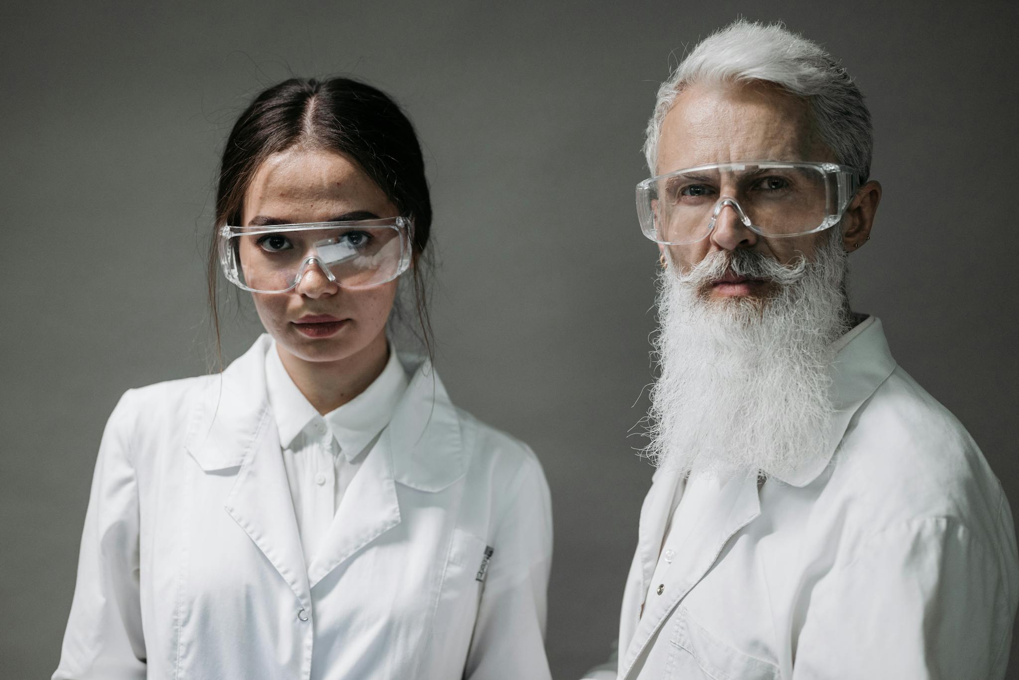 Two scientists wearing lab coats and safety goggles pose confidently.